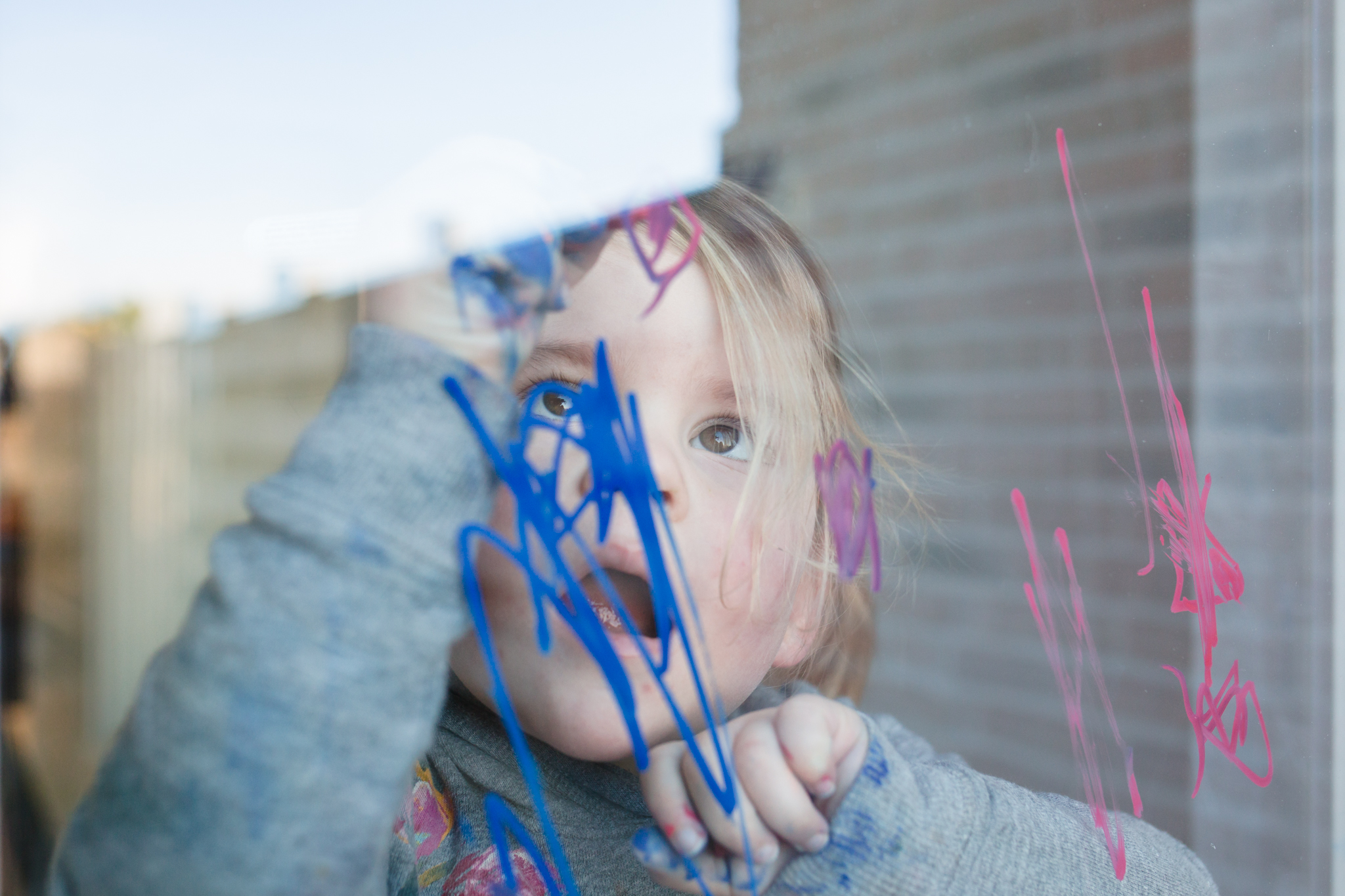Meisje maakt met krijtstiften van edding een tekening op de raam, day in the life fotografie