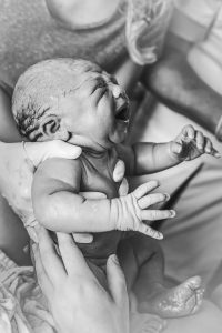 Verloskundige houdt baby vast die net geboren is om aan de moeder te laten zien