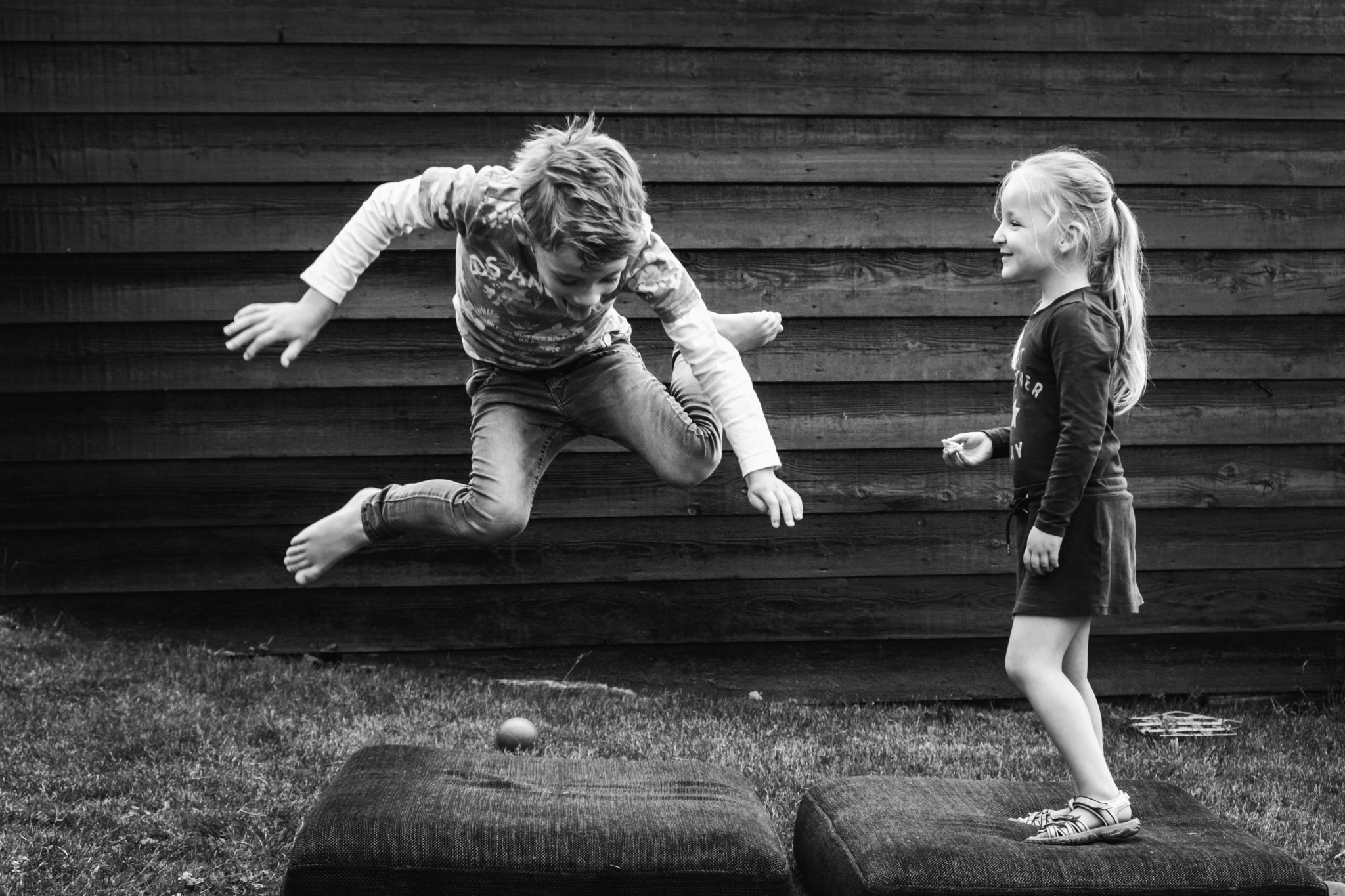 Jongen en meisje spelen samen in de tuin en springen op oude kussens
