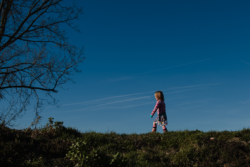 meisje loopt op een dijk met een blauwe lucht op de achtergrond. Foto voor het thema blauwe maandag.